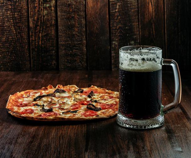 Taza de cerveza y pizza sobre fondo de madera oscura
 - Foto, imagen