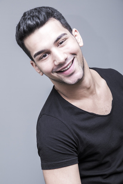 Young and handsome middle eastern man in black t-shirt on grey background, studio portrait - Фото, зображення