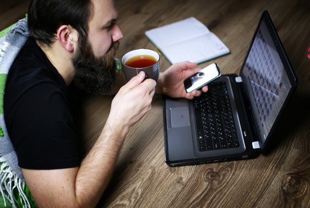 бородатий красивий чоловік лежить на підлозі, загорнутий в плетений, і робочий ноутбук
 - Фото, зображення