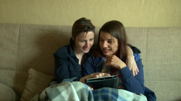 Lesbian girls using tablet, kissing, smiling and laughing on the sofa - Felvétel, videó
