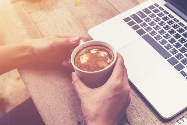 fiatal üzleti ember keze gazdaság csésze kávét, és segítségével a laptop számítógép  - Fotó, kép