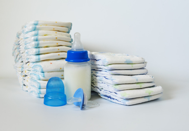Pila de pañales desechables para bebés, chupete y termómetros electrónicos sobre fondo blanco
. - Foto, Imagen