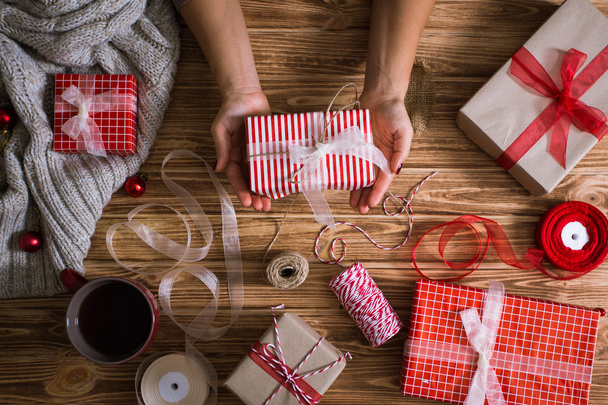 Las manos femeninas envuelven los regalos de Navidad en papel y los atan con hilos rojos y blancos
 - Foto, imagen