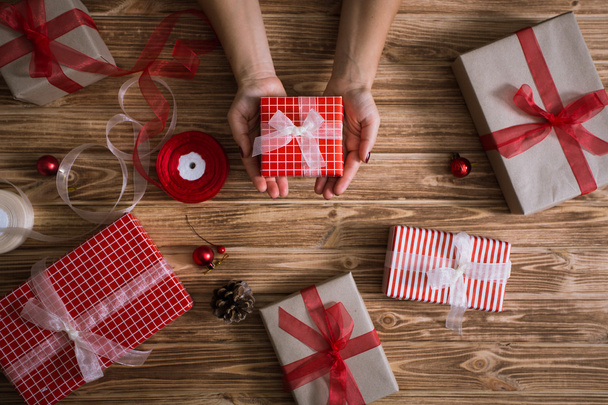 Vrouwelijke handen verpakking xmas geschenken in papier en koppelverkoop met rode en witte draden - Foto, afbeelding
