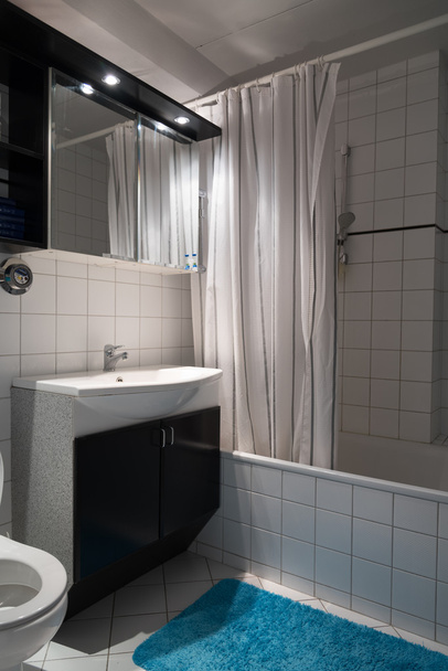 Небольшой санузел в квартире с ванной, туалетом, раковиной и шкафом с бирюзовым ковриком
 - Фото, изображение