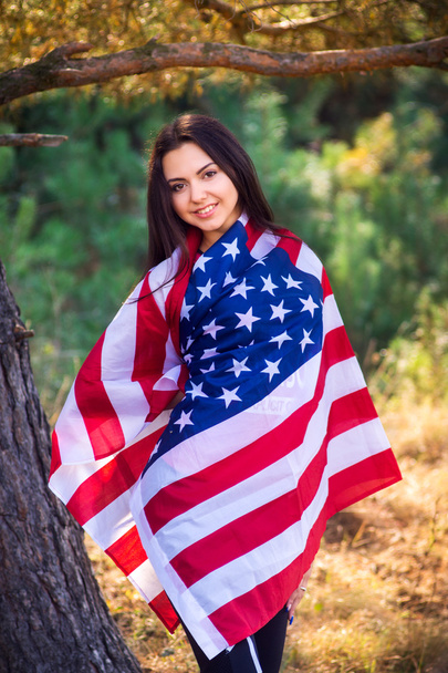 Beautiful model poses with the flag of the USA in the summer park - Photo, image