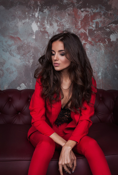 Retrato de uma jovem senhora de negócios sexy em terno vermelho no sofá escuro
 - Foto, Imagem