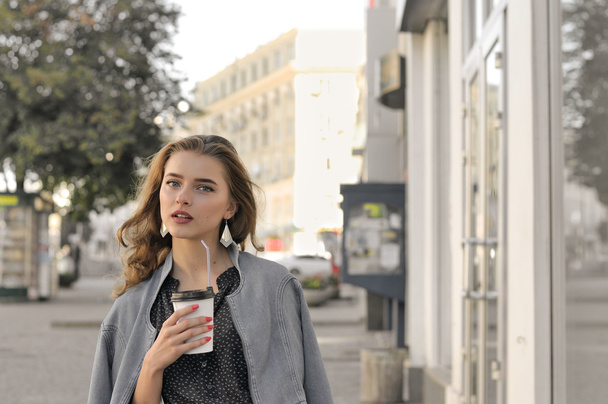 Girl goes on the sidewalk and drinking coffee - Fotó, kép