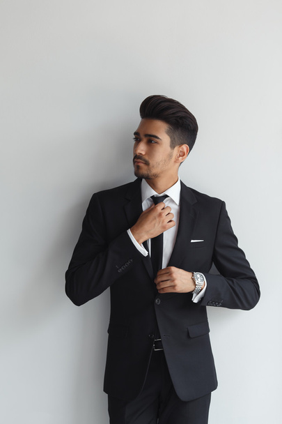 Making business look good. Confident young man in formal wear adjusting his necktie and looking away while standing against grey background - Photo, Image