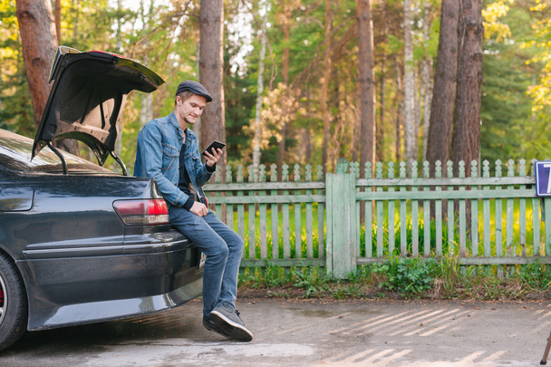 Young man sitting in the car trunk on the roadside - Zdjęcie, obraz