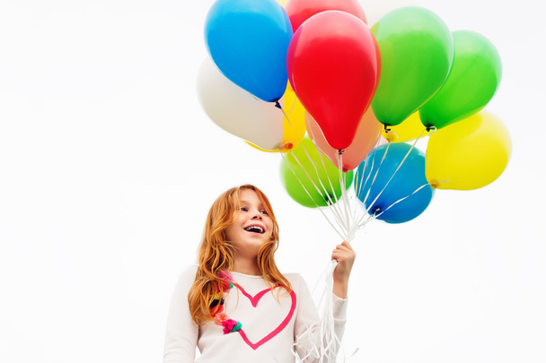 Heureuse petite fille de 8-9 ans aux cheveux roux tenant des ballons d'hélium colorés
 - Photo, image
