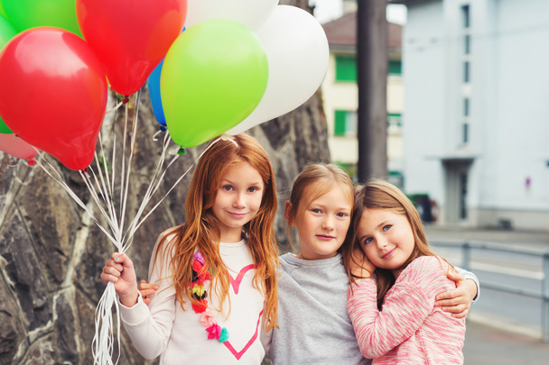 Außenporträt von 3 niedlichen kleinen Mädchen mit bunten Luftballons, die Sweatshirts tragen - Foto, Bild
