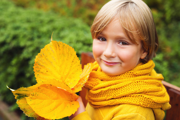 Otoño de cerca retrato de niño adorable con hojas, vistiendo sudadera amarilla cálida y bufanda de punto
 - Foto, imagen