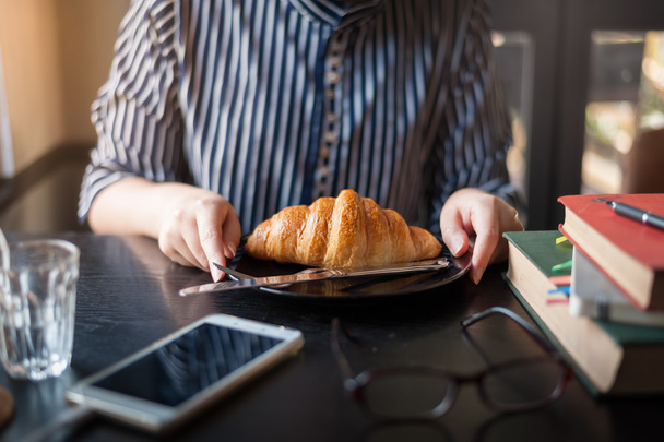Nainen syö croissantia kahvilassa.
 - Valokuva, kuva