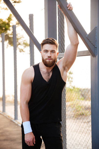 Handsome bearded sportsman in sportswear and wristband standing outdoors - 写真・画像