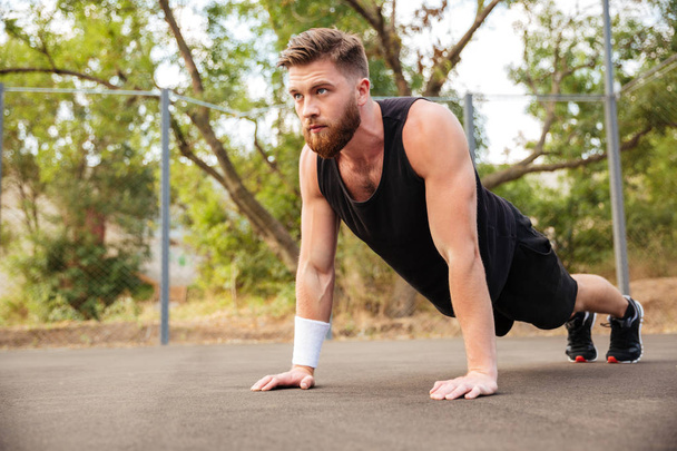 Attractive bearded sportsman doing push-ups outdoors - Photo, image