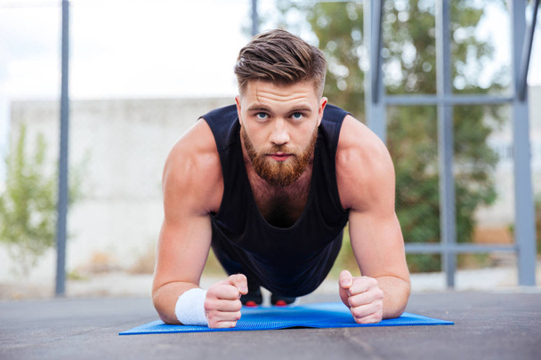 Sportsman doing plank exercise on blue fitness mat during workout - Photo, image