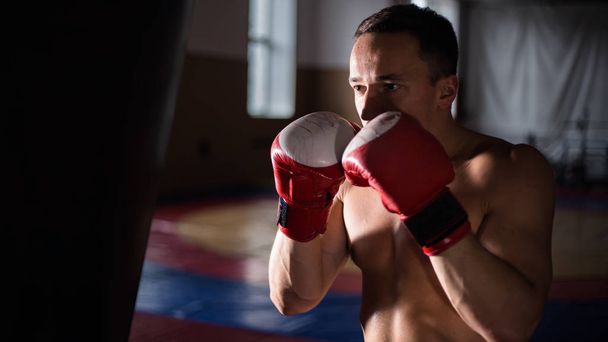 Combattente pratica alcuni calci con sacco da boxe un uomo su sfondo scuro. allenamento sul sacco da boxe. formazione di pugilato
 - Foto, immagini
