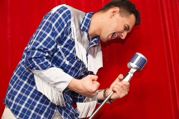 νεαρός άνδρας τραγουδά με το μικρόφωνο στα χέρια του - Φωτογραφία, εικόνα