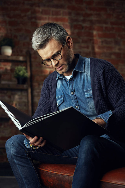 Portrait of handsome man with gray hair in studio loft reading a book - Foto, Imagen