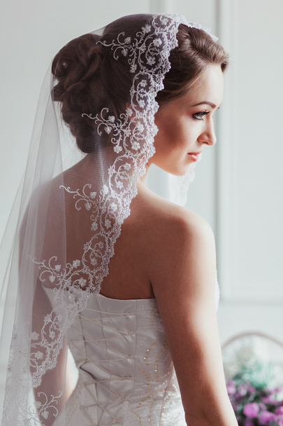 schöne Braut mit Mode Hochzeitsfrisur - auf weißem Hintergrund. Porträt einer jungen Frau. Studioaufnahmen. Mädchenschleier über ihrem Gesicht - Foto, Bild