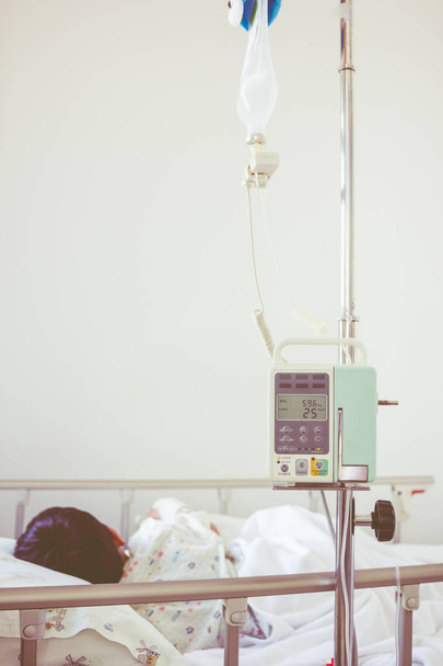 Asiático niño acostado en cama enferma con bomba de infusión intravenosa goteo IV
 - Foto, imagen