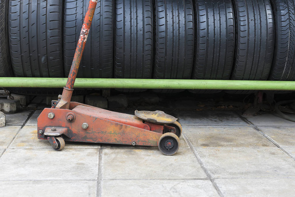 The old floor jack with the car used tire stack background. - Photo, Image