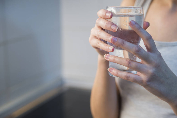 Happy beautiful young woman drinking water. Smiling caucasian female model holding transparent glass in her hand. Closeup. Focus on the arm - Fotoğraf, Görsel