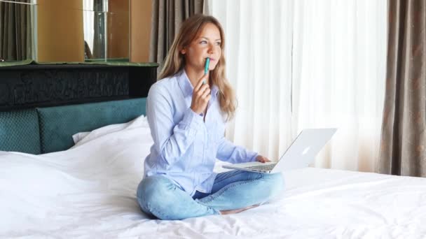 Beautiful caucasian woman working on laptop in the bedroom. Young cute girl using macbook and smiling. Nice happy teen seating on the bed and preparing to exams. Sunny morning. - Imágenes, Vídeo