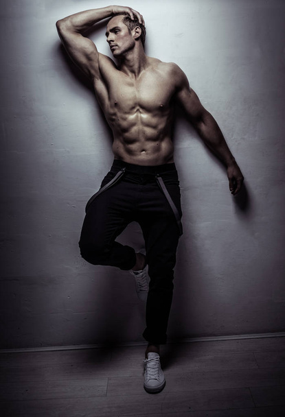 Мускулистый атлет молодой человек позирует над светло-серой стеной
 - Фото, изображение