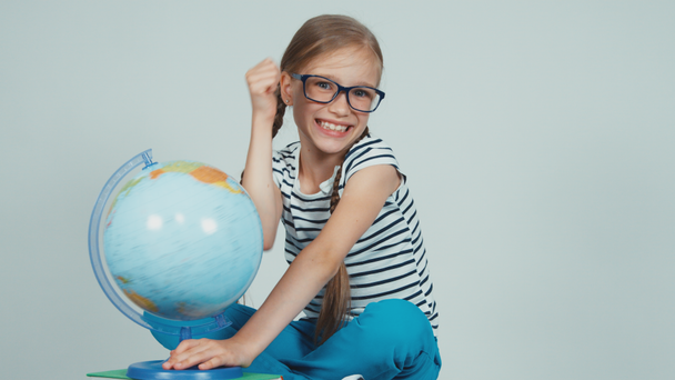 Шкільна дівчина обертає свій глобус і посміхається на камеру ізольовано на білому. Палець вгору. гаразд
 - Кадри, відео