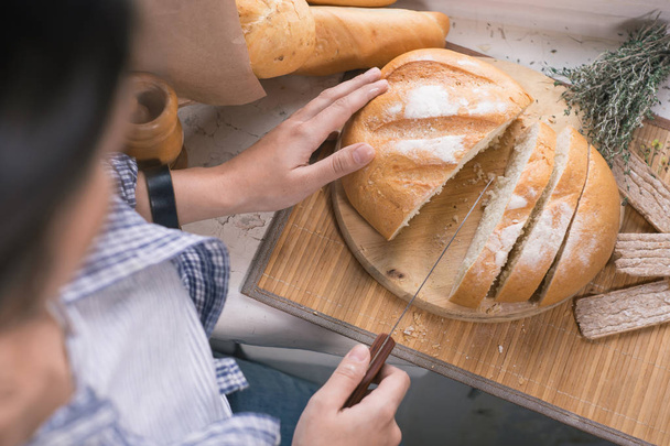 girl cuts the white bread on a wooden board - Zdjęcie, obraz