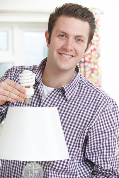 Man Putting Low Energy Lightbulb Into Lamp At Home - Foto, Imagem