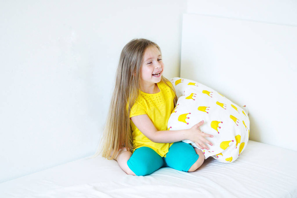 Schattig meisje speelt met het kussen op het bed in haar slaapkamer - Foto, afbeelding