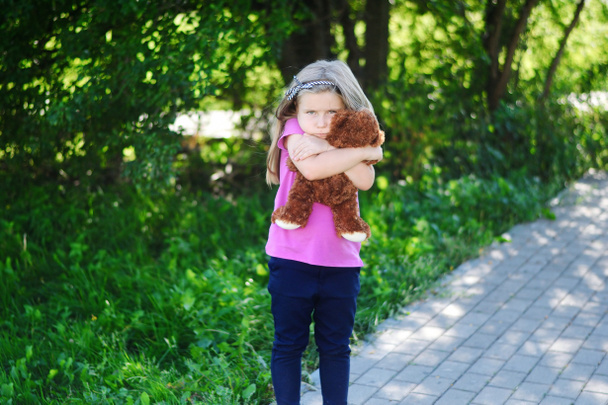 Αξιολάτρευτο κορίτσι λυπημένο με αρκουδάκι στο πάρκο. - Φωτογραφία, εικόνα