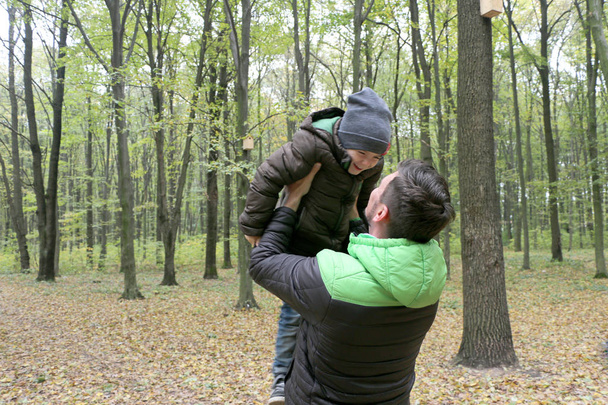 father holds his small cute clever son on nature in the forest - Фото, зображення