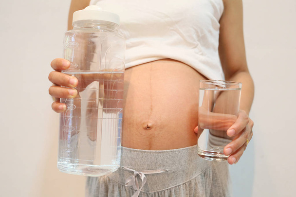 妊娠中の女性は、手に飲み物の水のガラスを保持します。. - 写真・画像
