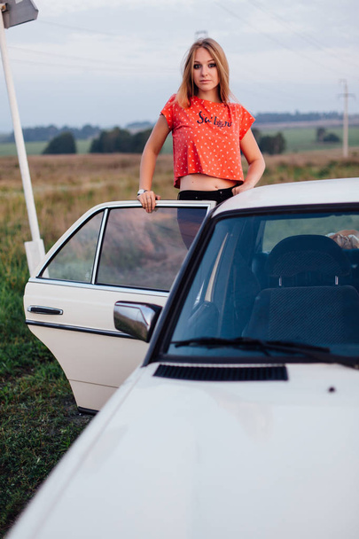 Portrait of a beautiful young woman standing near retro car - 写真・画像