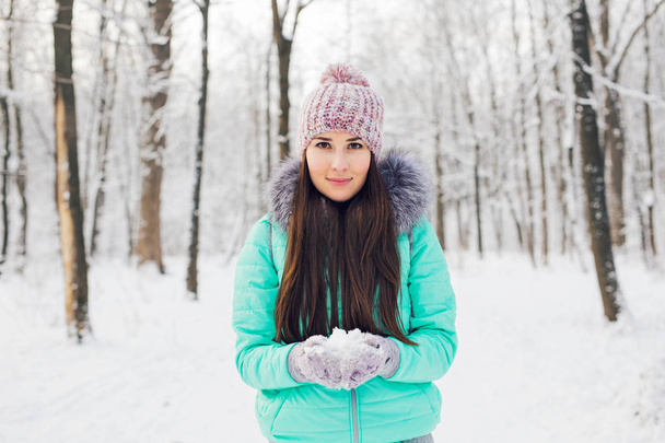 Nuori nainen pitää käsissään luonnollista pehmeää valkoista lunta tehdäkseen lumipallon, hymyillen kylmän talvipäivän aikana metsässä, ulkona
. - Valokuva, kuva