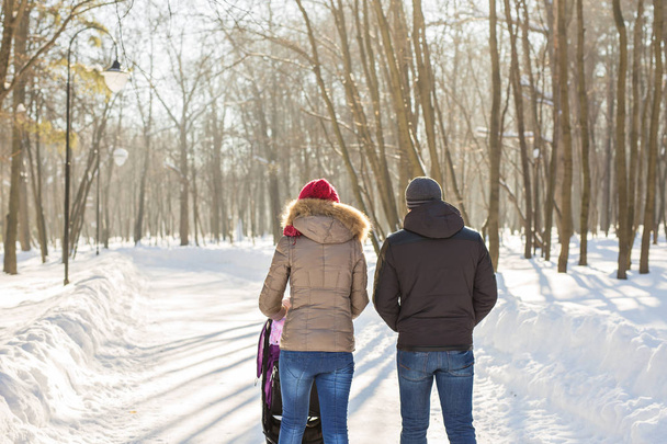 Feliz jovem família caminhando no parque no inverno. Os pais carregam o bebê em um carrinho de bebê através da neve
. - Foto, Imagem