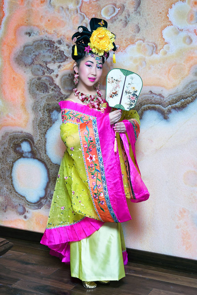 Geisha. Mujer joven en kimono amarillo con abanico y flor en el pelo
. - Foto, Imagen