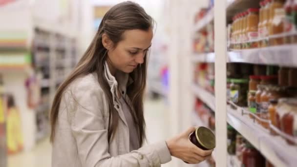 Young woman is choosing sauce in jar at the shopping center. - Кадры, видео