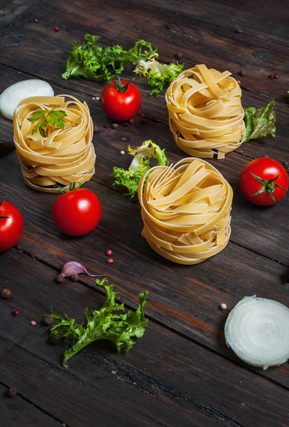 Italian food cooking ingredients. Pasta, tomatoes, onion on dark wooden background - Φωτογραφία, εικόνα