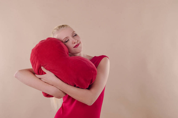 Όμορφη νεαρή γυναίκα σε ένα φωτεινό κόκκινο κρυψίνους φόρεμα που αγκαλιάζει ένα plu - Φωτογραφία, εικόνα