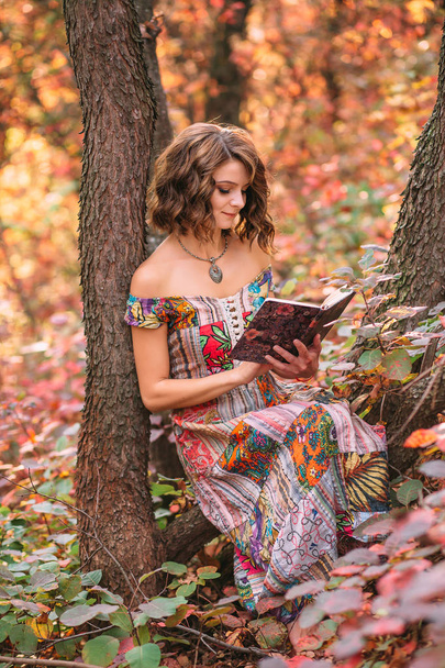 Jovem menina bonita sentada sob uma árvore com um livro
 - Foto, Imagem
