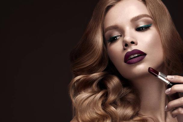 Beautiful blonde in a Hollywood manner with curls, dark lips, lipstick in hand. Beauty face and hair. - Foto, immagini