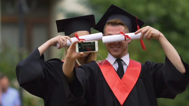 Smiling female and male graduates shooting video on smartphone, having fun - Footage, Video