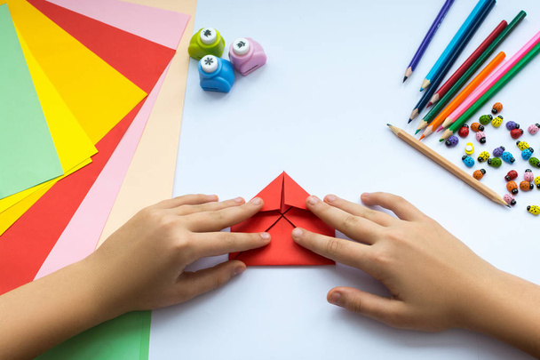 Children's hands do origami  bird from red paper. - Фото, изображение