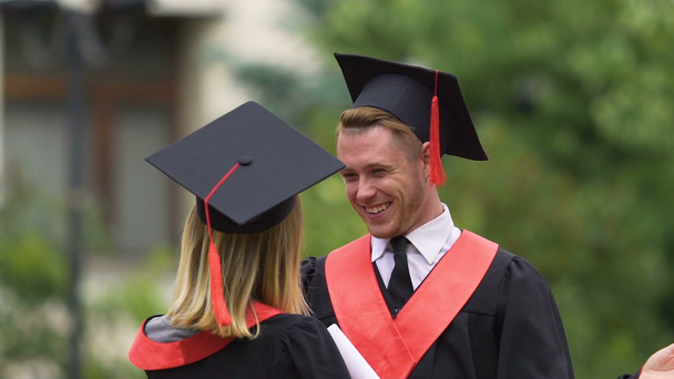 Radosna para w akademickich sukienki przytulanie i śmiejąc się, szczęśliwa przyszłość, edukacja - Materiał filmowy, wideo