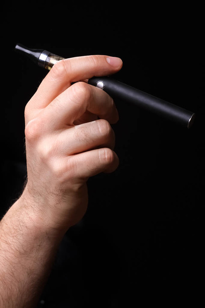 A kezében egy fekete háttér elektronikus cigaretta - Fotó, kép
